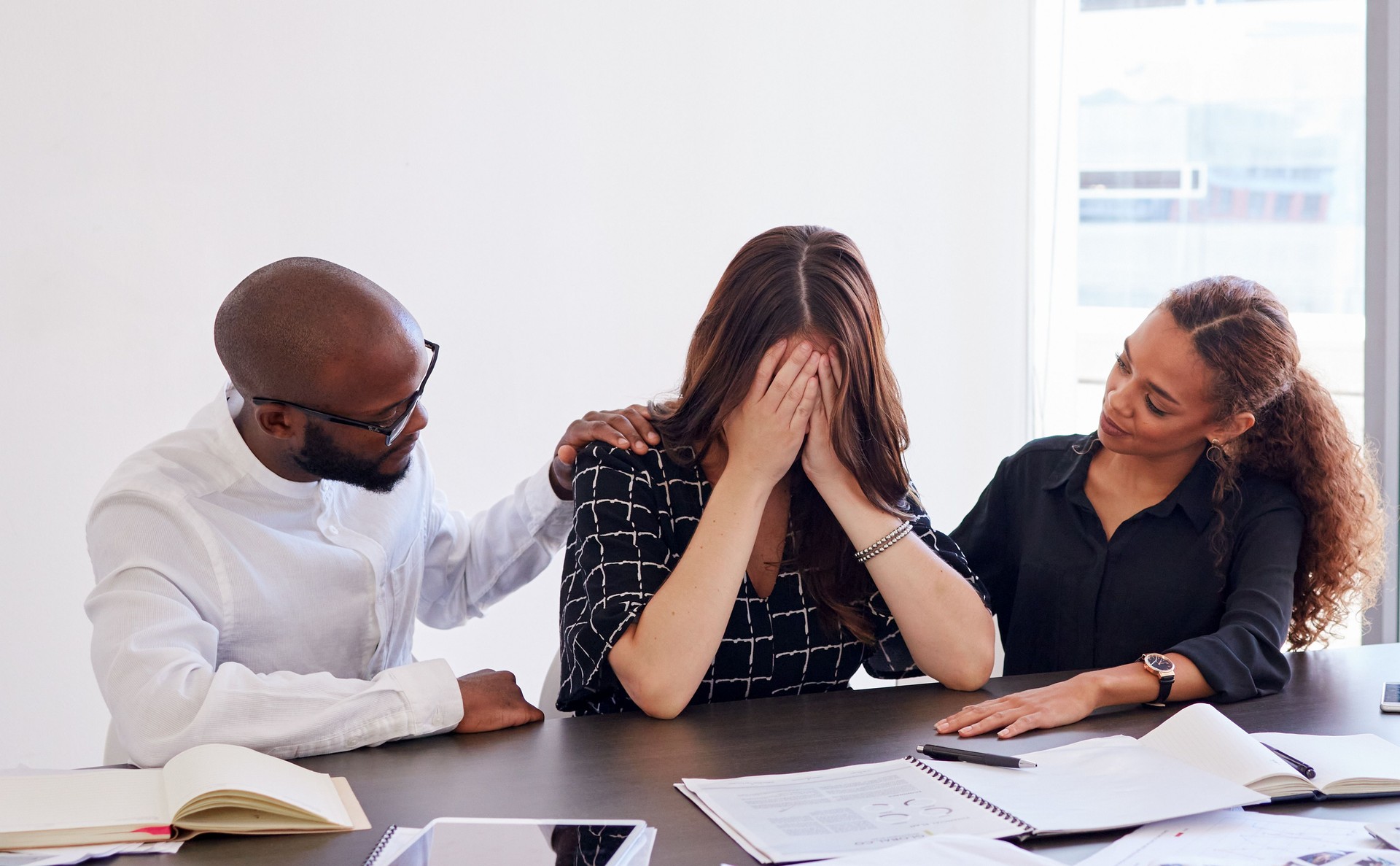 Shot of a young businesswoman in distress being comforted by her coworkers